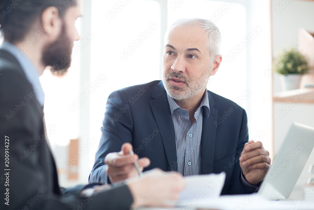 Mature businessman discussing contract with his coworker at office Mature businessman discussing contract with his coworker at office