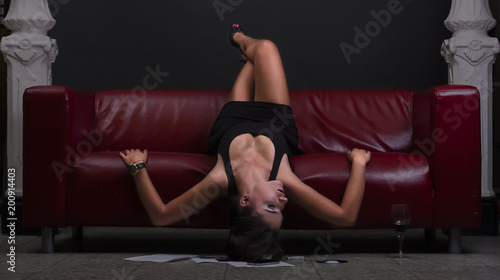 Beautiful young woman in black dress lying on leather red sofa