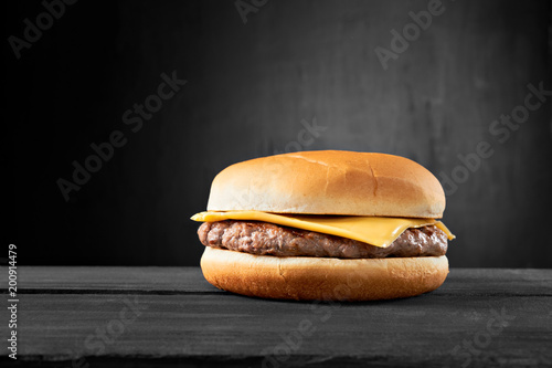Plain beef burger with cheese on wooden table isolated on black background.