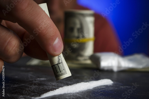 Drug addict man using narcotics, sniffing cocaine lines white powder with rolled dollar banknote