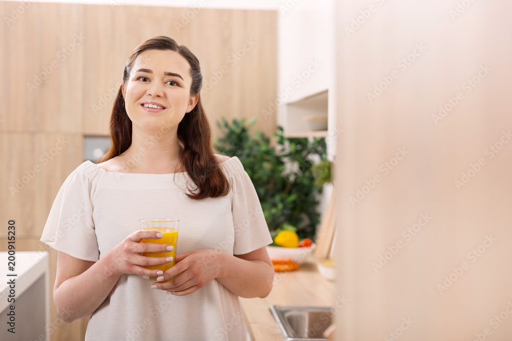 Great morning. Pensive jovial woman grinning to camera while carrying glass of orange juice Great morning. Pensive jovial woman grinning to camera while carrying glass of orange juice