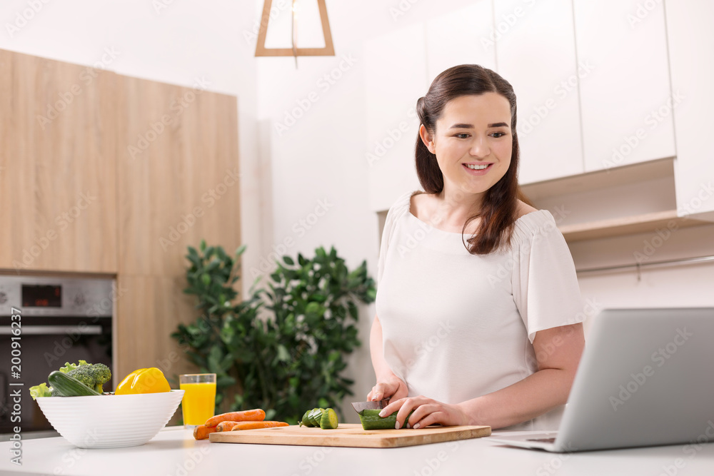 New material. Happy female blogger examining video while cutting vegetable