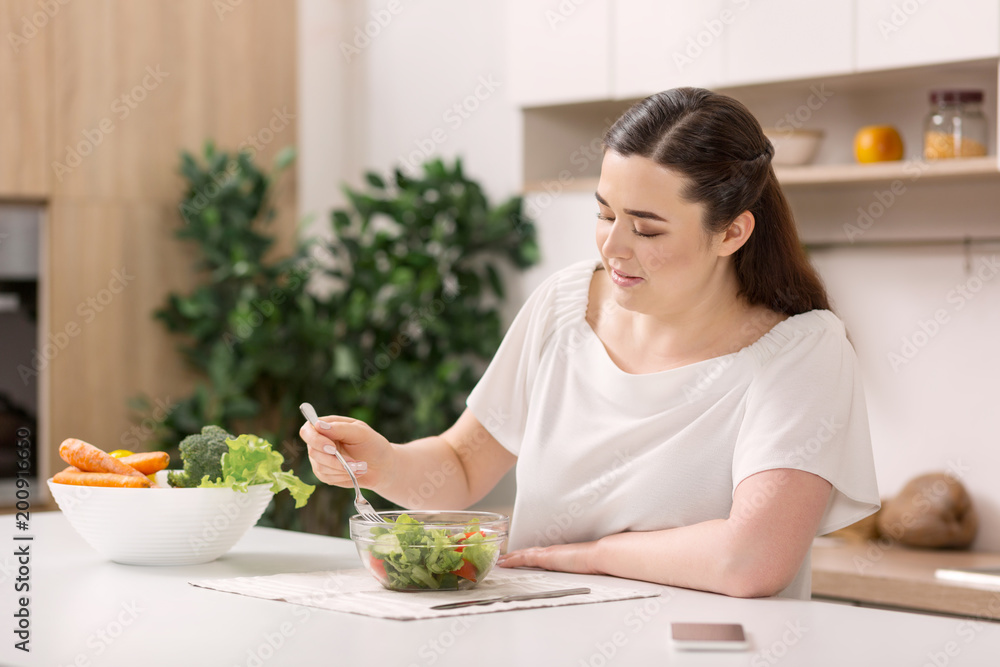 Best food. Upset concentrated woman looking down and tasting salad Best food. Upset concentrated woman looking down and tasting salad