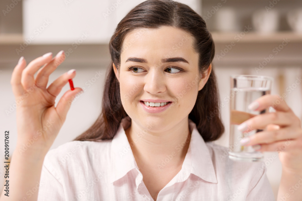 Treat you body. Appealing vigorous woman looking at pill while holding glass of water Treat you body. Appealing vigorous woman looking at pill while holding glass of water