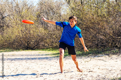 Athletic teenage boy is enthusiastically throwing frisbee disk