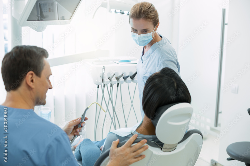 Obraz premium Dental work. Inspired skilled dentist wearing a mask and looking at her patient