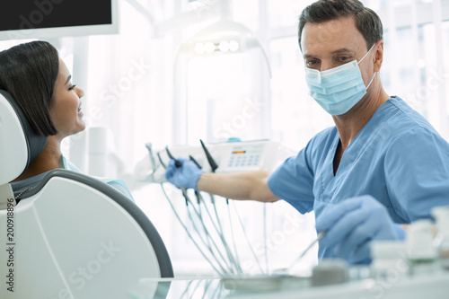 My work. Concentrated dark-haired dentist wearing a uniform and holding an instrument