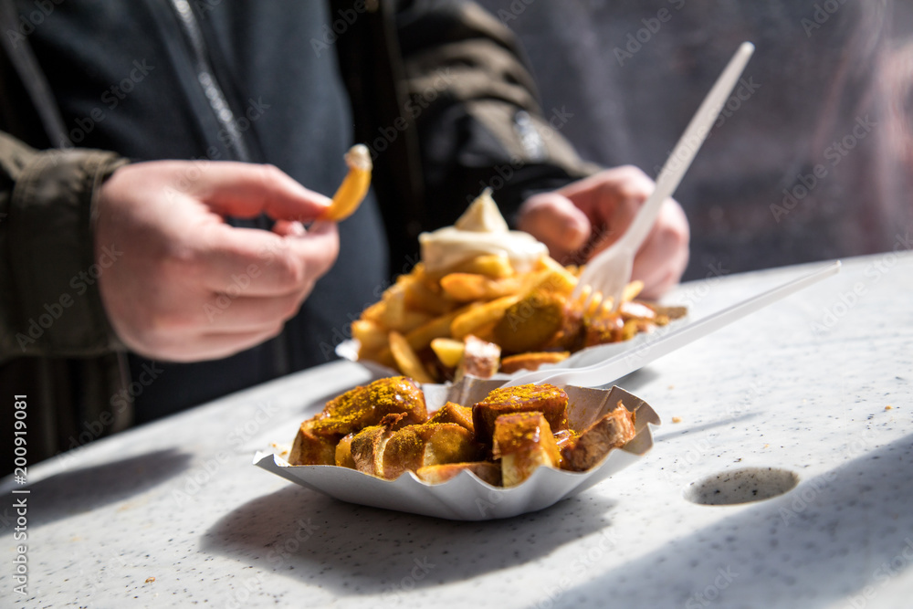 Mann isst Currywurst Pommes Mayo draußen am Wochenmarkt Imbiss