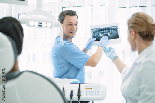 Great results. Content skilled dentist talking with his colleague and showing teeth on the screen