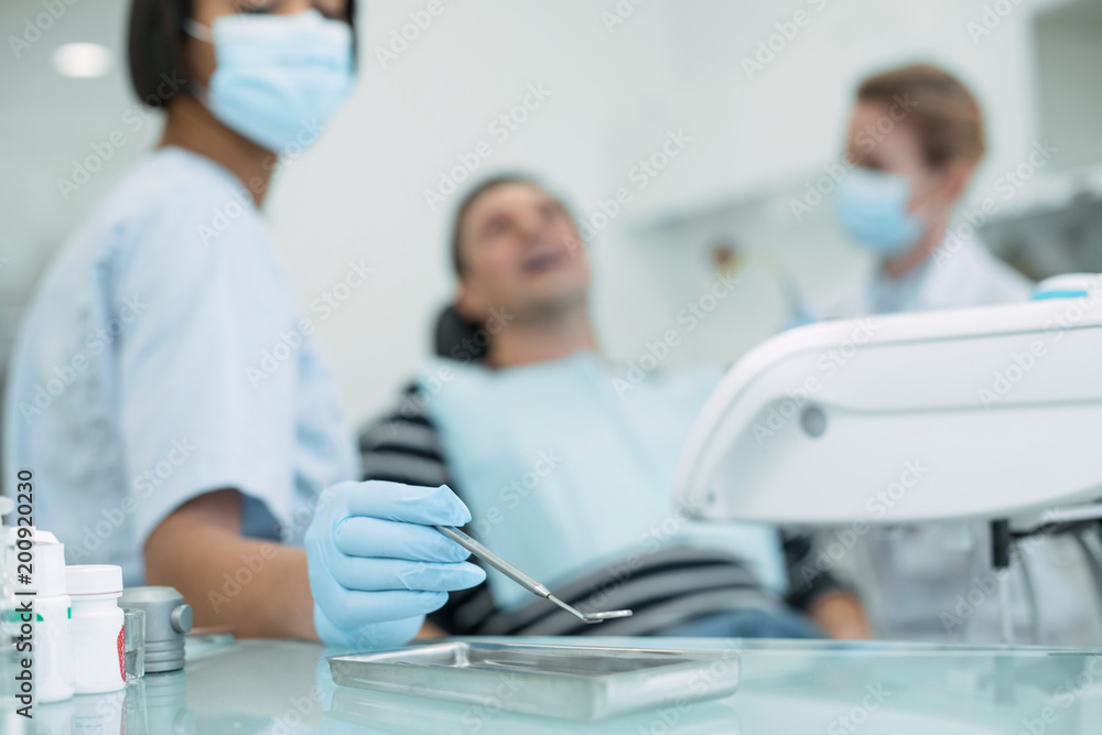 Our routine work. Determined skilled dentist holding an instrument and the patient sitting in the chair Our routine work. Determined skilled dentist holding an instrument and the patient sitting in the chair
