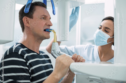 Modern device. Nice concentrated man opening his mouth and having a dental device in it