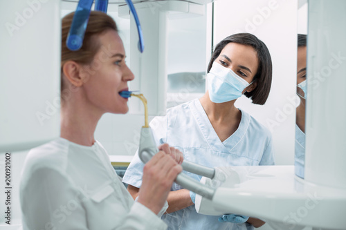 Under control. Alert experienced dentist wearing a uniform and watching her patient