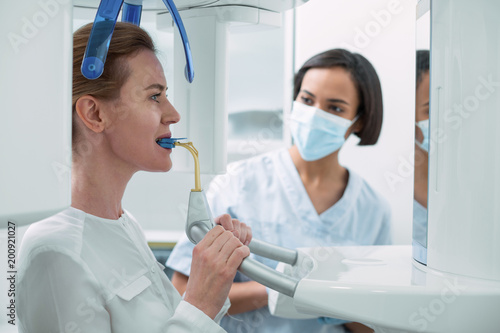 Controlling the process. Inspired experienced dentist wearing a uniform and watching her patient