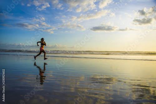 silhouette of young Asian sport runner woman in running workout training at sunset beach with orange sunlight reflection on the sea water