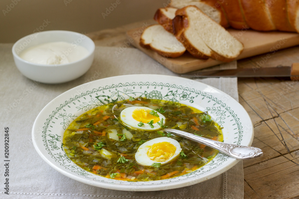 Vegetarian sorrel soup with egg, served with sour cream and bread. Rustic style. Vegetarian sorrel soup with egg, served with sour cream and bread. Rustic style.