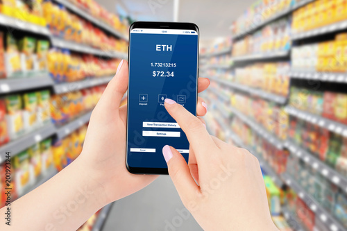Female paying bill in supermarket with smartphone using Ethereum cryptocurrency. Blockchain shopping concept.