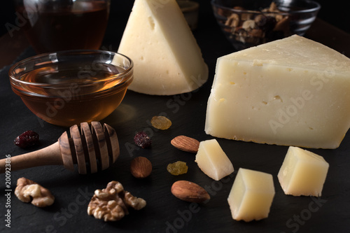 Greek cheese graviera and a slices on black stone board with nuts, honey and herbs. photo