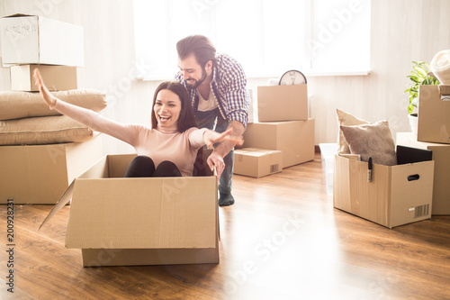 Attractive woman is sitting on the box. Her man is pushing her so she can ride. This people look happy and satisfied