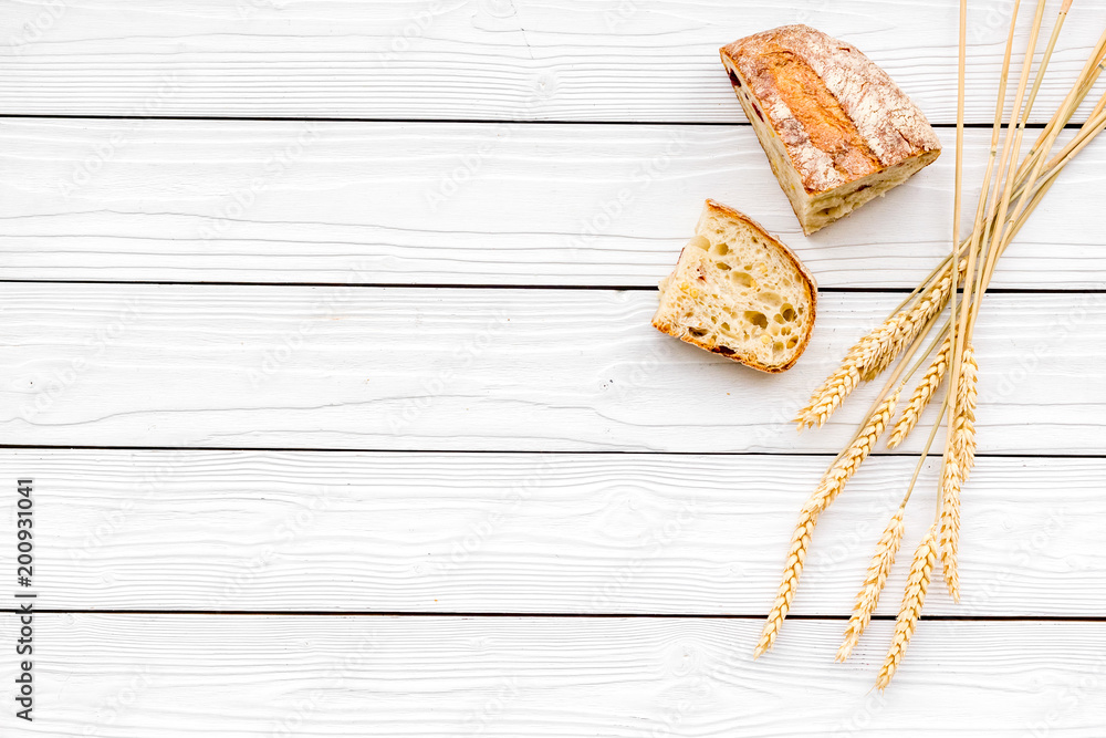 Appetizing fresh bread concept. Sliced loaf near ears of wheat on white wooden background top view copy space Appetizing fresh bread concept. Sliced loaf near ears of wheat on white wooden background top view copy space
