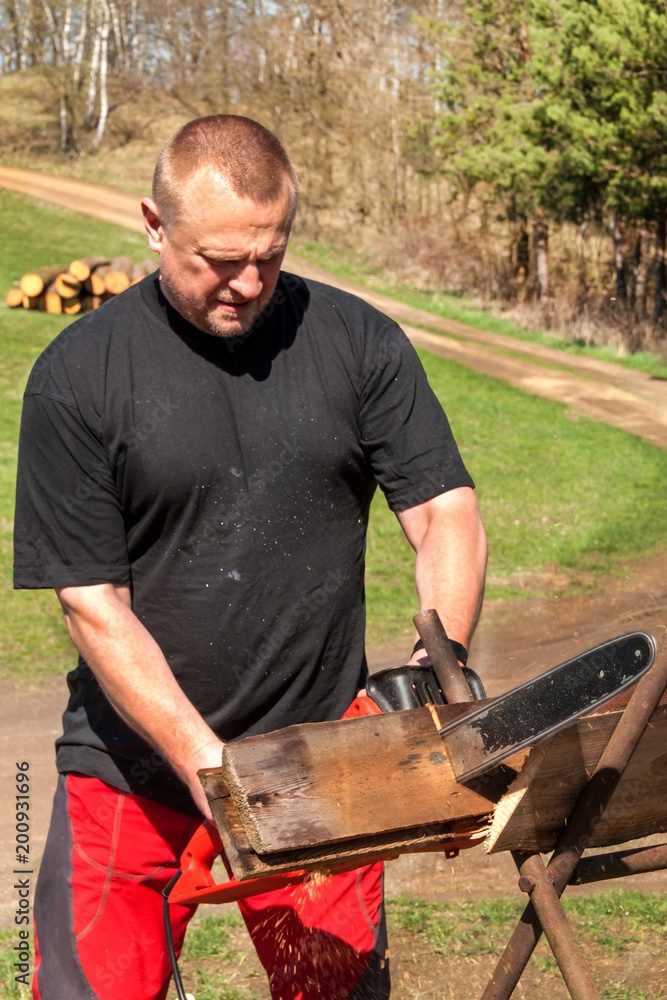 Man cutting with electric chain saw. Work on the farm. Wood preparation for heating. The woodcutter works with the saw. Man cutting with electric chain saw. Work on the farm. Wood preparation for heating. The woodcutter works with the saw.