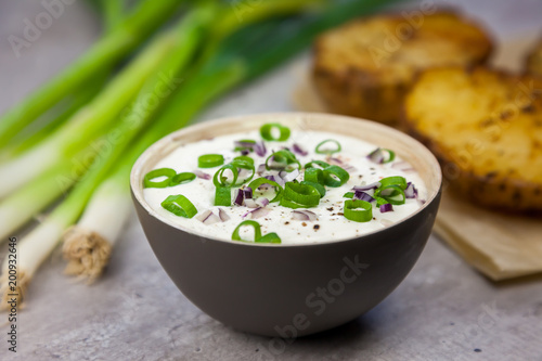 Bowl with curd decorated with spring onion. Baked jacket potatoes and spring onion on the background