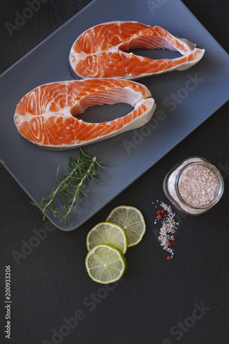  Close-up photo of fresh salmon fish with sea salt and lime slices on black table background. 