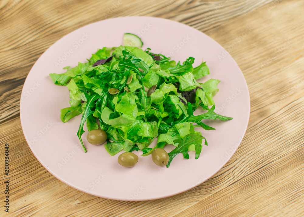 Fresh lettuce leaves, basil, arugula in a glass bowl on a wooden background. Preparation of a vegetarian vegetable salad. Fresh lettuce leaves, basil, arugula in a glass bowl on a wooden background. Preparation of a vegetarian vegetable salad.