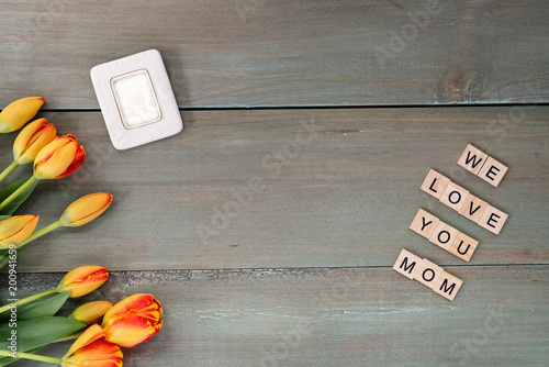 Colorful tulips and small picture frame on weathered green planks. Tile letters with sentiment for Mother's Day.