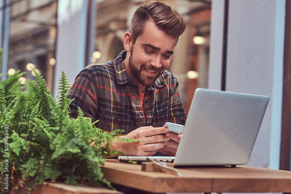 Portrait of a smiling fashionable bearded male with a stylish haircut, dressed in a flannel shirt, sitting in a cafe outdoors. Portrait of a smiling fashionable bearded male with a stylish haircut, dressed in a flannel shirt, sitting in a cafe outdoors.