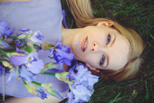 Attractive young girl with blonde dren hair and natural make-up smelling blue purple iris flowers lying on grass outdoors, tenderness and softness on nature background photo