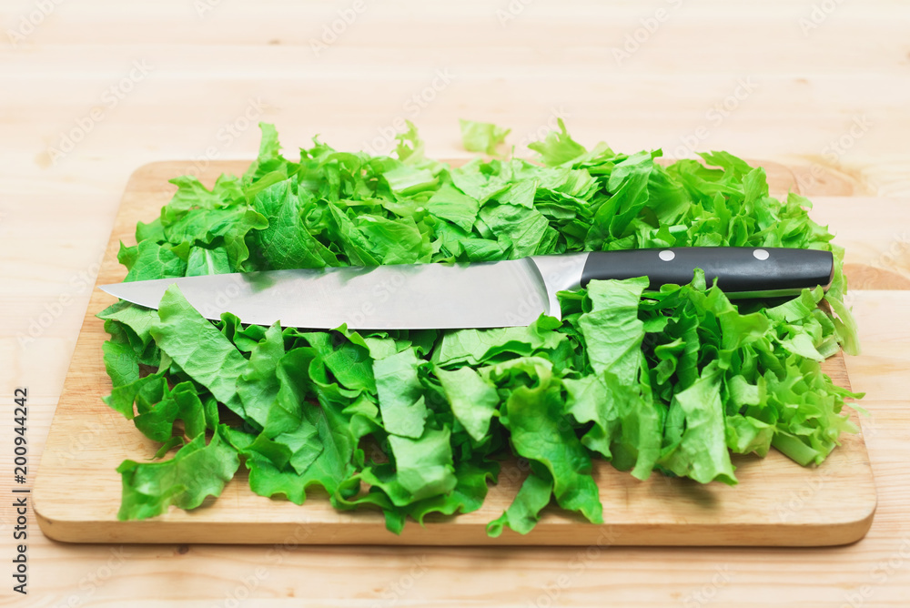 Close-up on a wooden table is a wooden cutting board on which lies the chopped lettuce leaves and on them lies a large cutting knife. The concept of self-cooking vegetarian food at home. Healthy Close-up on a wooden table is a wooden cutting board on which lies the chopped lettuce leaves and on them lies a large cutting knife. The concept of self-cooking vegetarian food at home. Healthy