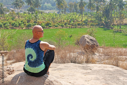 Bald Man is a tourist and photographer in Hampi, sits on a rock and looks into the distance. Large stones Hampi on the side of the village of Anegundi and Virupapur Gaddi. Large stones photo