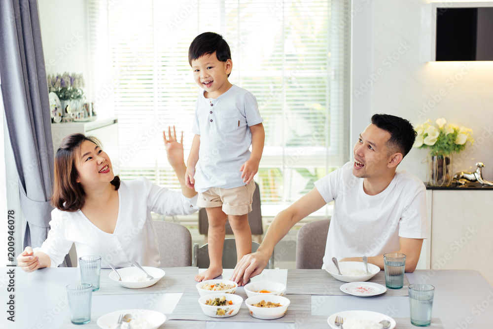Asian family watching their kid as he is determined and proud to finally stand on the dining table Asian family watching their kid as he is determined and proud to finally stand on the dining table
