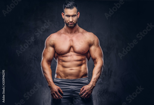 Portrait of a shirtless tall huge male with a muscular body with a stylish haircut and beard, in a sports shorts, posing in a studio.