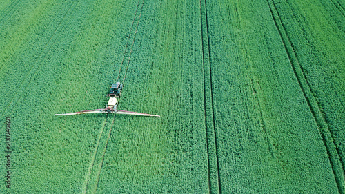 Aerial view Farm machinery spraying chemicals on the large green field, agricultural spring background.