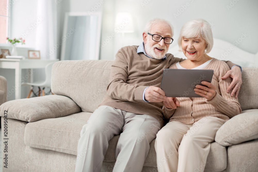Modern device. Joyful aged people smiling while looking at the tablet screen - obrazy, fototapety, plakaty 