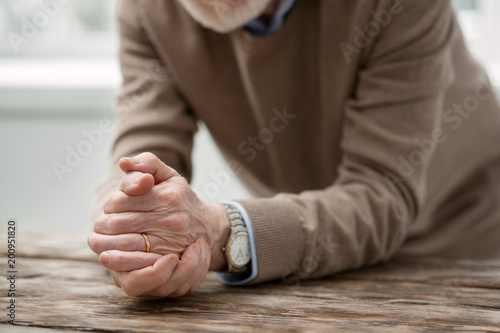 Sad feelings. Nice aged man putting his hands on the table while being all alone
