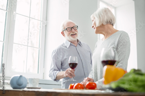 Pleasant drink. Cheerful nice aged man talking to his wife while enjoying wine