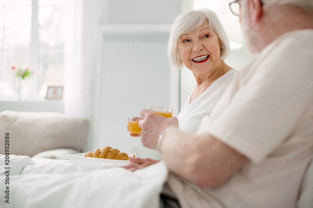 Delicious meal. Joyful positive aged couple having breakfast while lying in bed Delicious meal. Joyful positive aged couple having breakfast while lying in bed