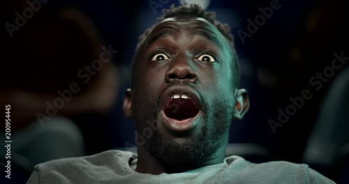 Young man reacts with a large gasp while watching a movie