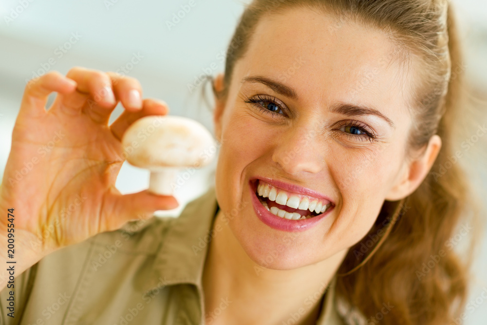 Happy young housewife holding mushroom in kitchen Happy young housewife holding mushroom in kitchen
