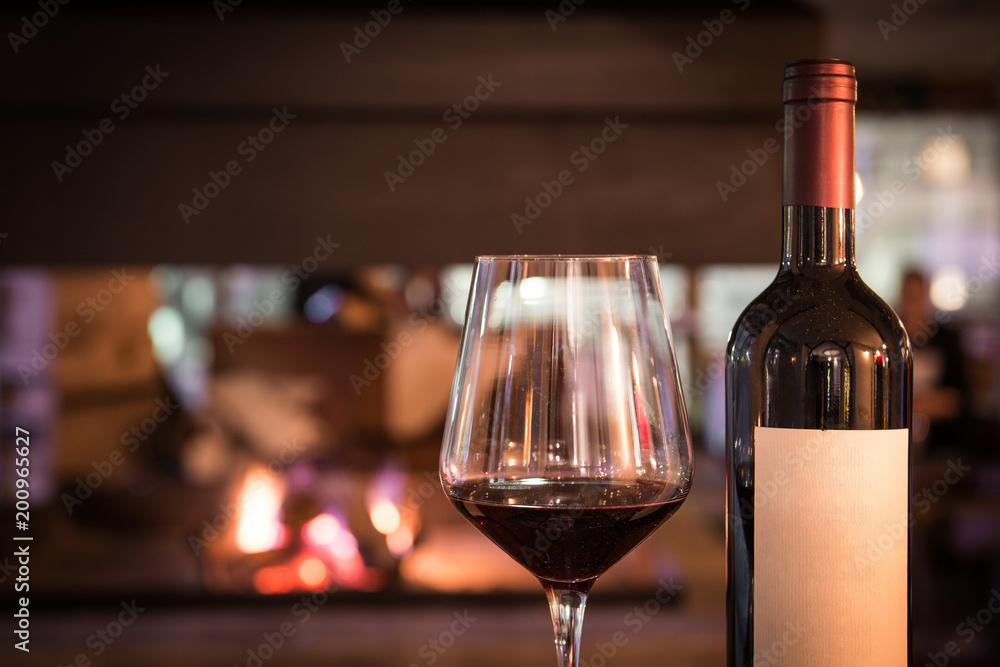 Glass red wine and bottle near a fireplace
