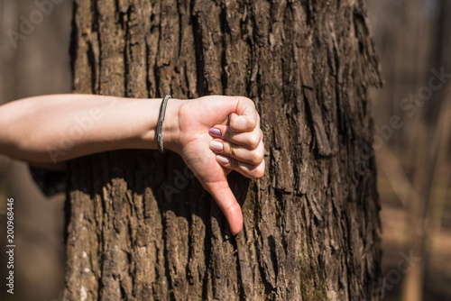 Female hand showing bad sign against a tree trunk in the forest