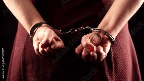submissive woman wearing a purple dress in leather handcuffs on black background