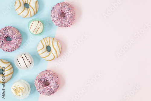 Sweet and colourful donuts and cupcakes glazed with sprinkles and frosting. Set of different type of cakes on the blue and pink background.