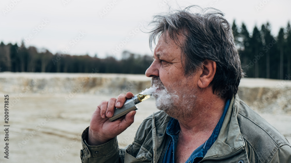 Old man with casual outfit is smoking an e-cigarette in forest area Stock  Photo | Adobe Stock