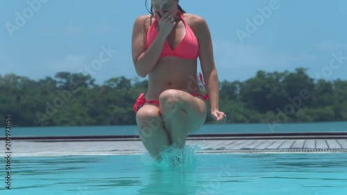SLOW MOTION, CLOSE UP: Playful woman does a cool cannonball jump into exotic island pool. Girl pinches her nose and jumps feet-first into beautiful emerald water, sending glassy water droplets flying.