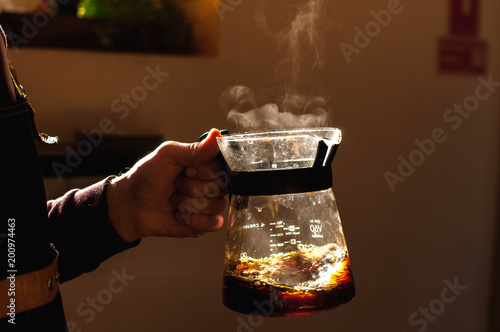 barista holds a drink in hand with a steam making alternative way of brewing coffee in the coffee shop hario v60 soft light background