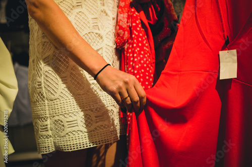Closeup on hands of a woman holding choosing clothes on shopping background. Modern consumerism lifestyle
