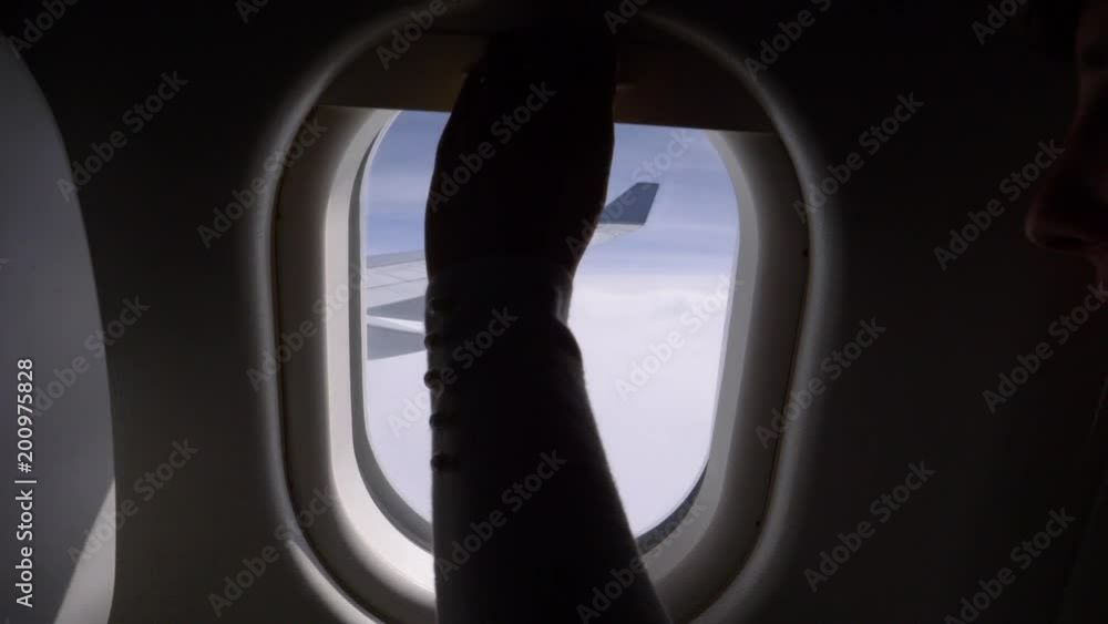 POV, CLOSE UP: Looking through the window of a large commercial airplane at cruising altitude before unknown woman closes the blinds. Cool shot of watching the aeroplane wing and the endless blue sky.